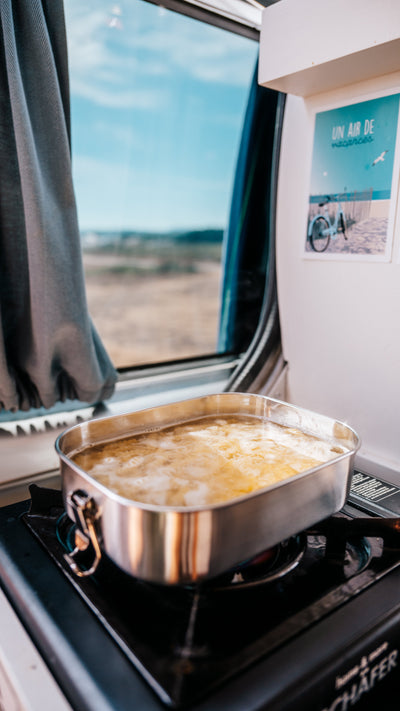 Pasta boiling in a stainless steel lunch box on a gas camping stove inside a van