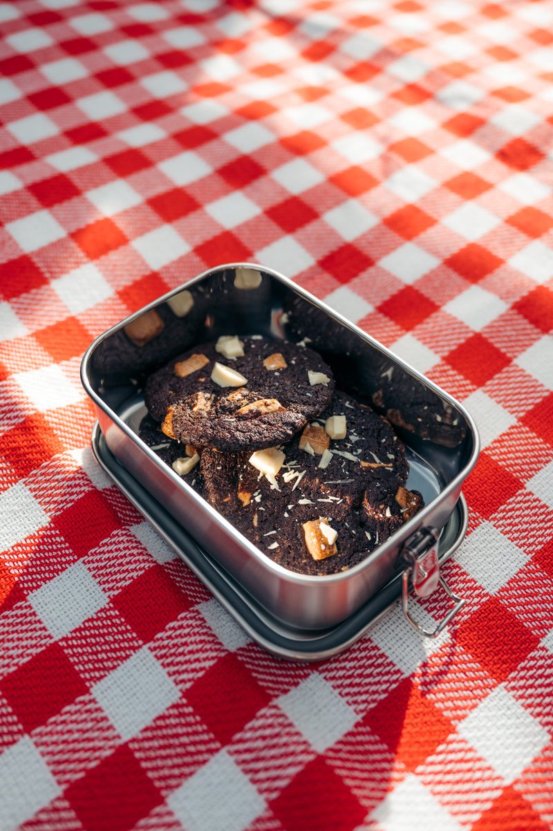 Open stainless steel lunch box on a checkered picnic blanket, filled with cookies