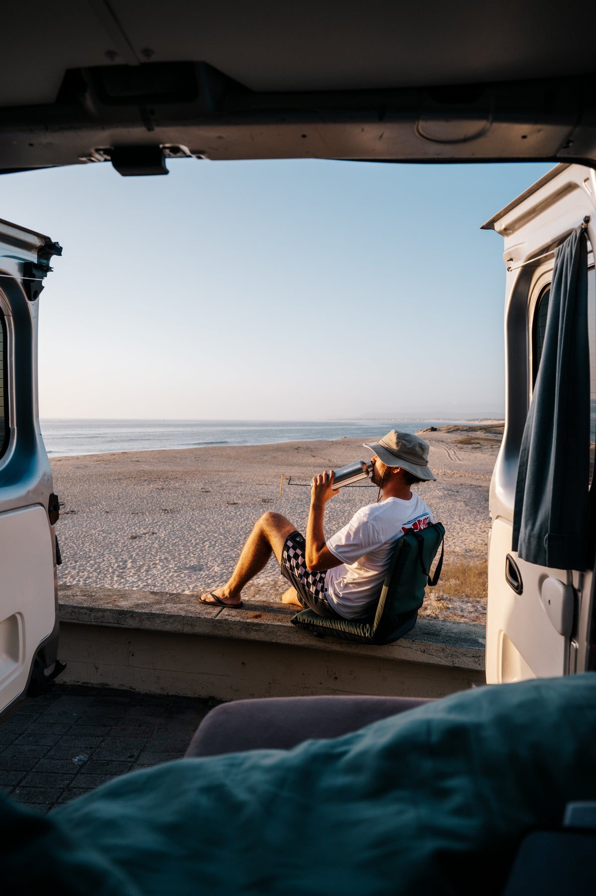 A man drinking from a Blockhuette stainless steel water bottle outside a van at the beach