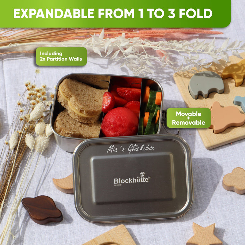 Open lunch box with two movable dividers, sandwiches, strawberries and cucumber, lid engraved Mia's Glücksbox in script