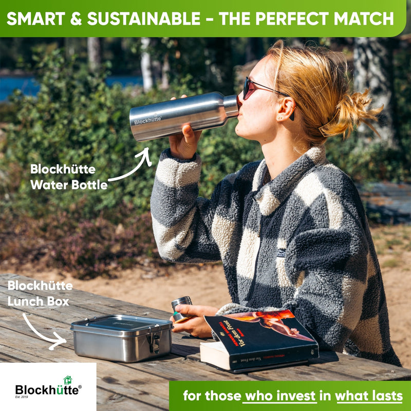 Woman in a checked fleece drinking from a Blockhütte water bottle at a picnic table, steel lunch box and book beside her