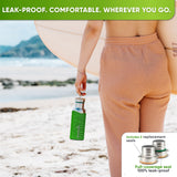 Woman carrying a surfboard along a beach, the 17 oz bottle in a bright green silicone sleeve hanging from her hand by the cap handle; inset: caps with replacement seals