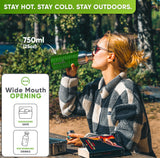 Woman in sunglasses and a checked fleece jacket drinking from the 25 oz bottle in a bright green silicone sleeve at a forest picnic table