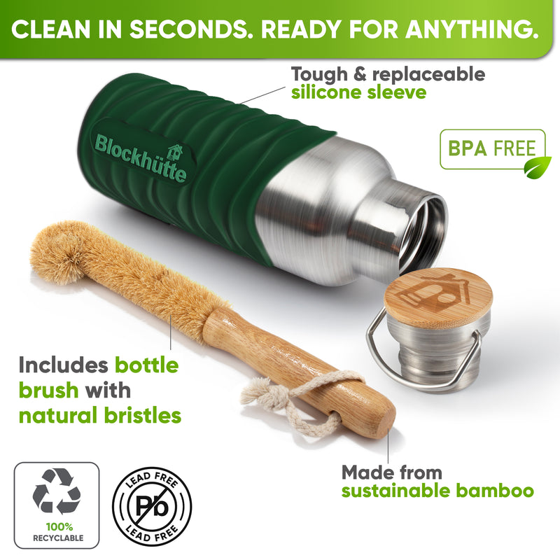Bottle in a dark green silicone sleeve lying on its side next to a bamboo bottle brush with natural bristles and the bamboo cap