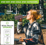 Woman in sunglasses and a checked fleece jacket drinking from the 25 oz bottle in a pink silicone sleeve at a forest picnic table