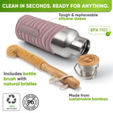 Bottle in a pink silicone sleeve lying on its side next to a bamboo bottle brush with natural bristles and the bamboo cap