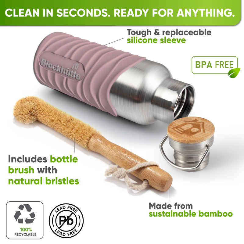 Bottle in a pink silicone sleeve lying on its side next to a bamboo bottle brush with natural bristles and the bamboo cap